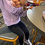 Kehlani is registered to the contest to win money with this photo: child, girl, smile, peace_sign, hoodie, dinosaur_design, sneakers, purple, black_leggings, chair, table, indoor, carpet, wooden_furniture, window, casual_clothing, happy, pose, person, young