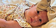 Kaisyn is registered to the contest to win money with this photo: baby, infant, face, headband, bow, floral_clothing, blanket, soft_texture, lying_down, cute, closeup, skin, sleepy, young_child, portrait, indoors, baby_girl, expression, peaceful, child