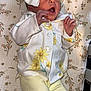 baby, infant, bow, yellow_pants, floral_jacket, yawning, blanket, crib, patterned_blanket, sleepwear, newborn, clothing, cute, baby_clothes, headwear, lying_down, indoors, soft_lighting, person, baby_sock