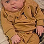 baby, infant, child, face, expression, clothing, brown_outfit, bear_design, hands, legs, sitting, indoor, blanket, soft_texture, cute, portrait, young_child, human, cozy, comfortable