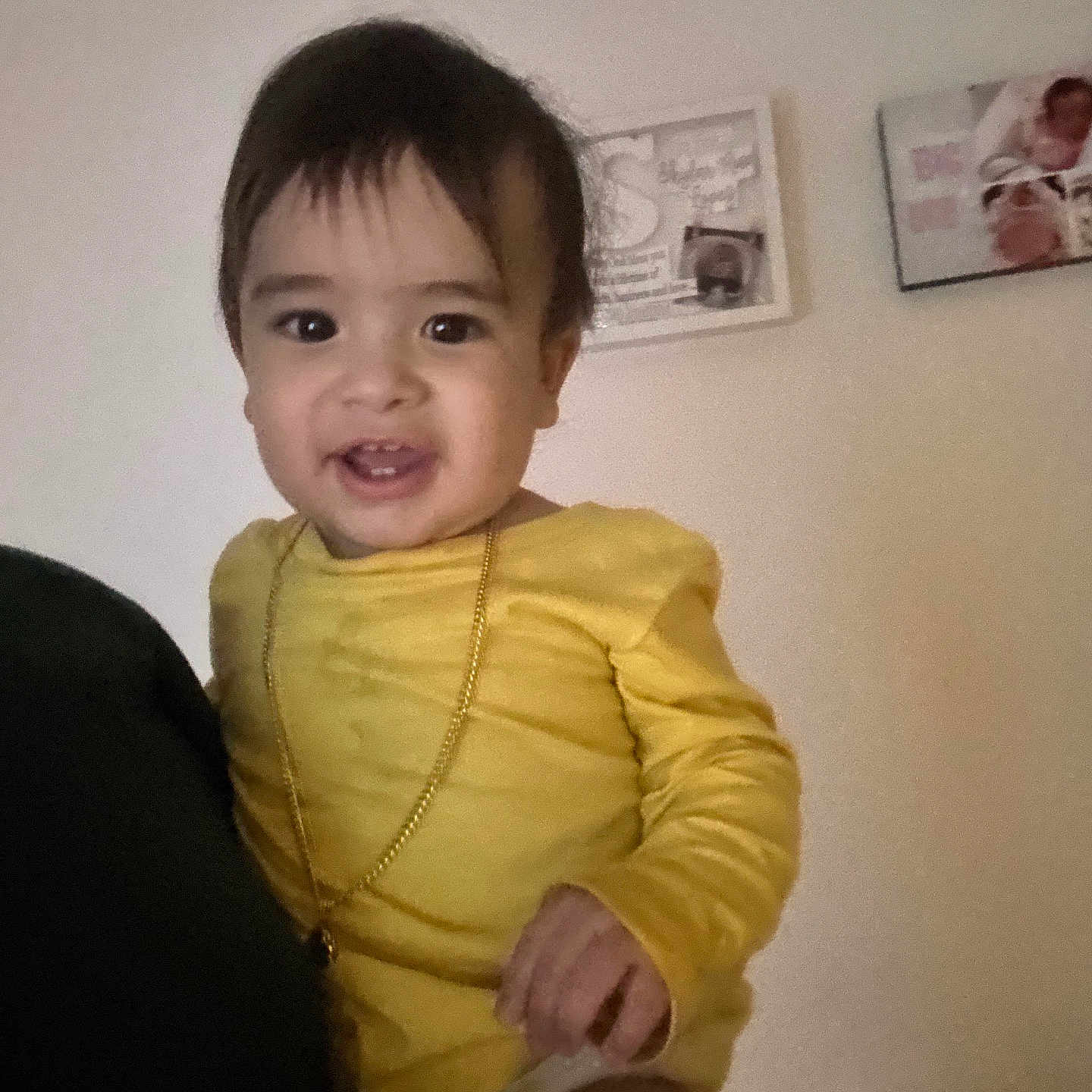 Larry Jr is registered to the contest to win money with this photo: adult_hand, baby, child, face, furniture, gold_chain, hand, happy, head, home, indoor, person, picture_frame, portrait, shoulder, sitting, smiling, toddler, wall, yellow_clothing