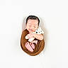 newborn, baby, sleeping, wrapped, brown_cloth, teddy_bear, crocheted_toy, soft_background, white, peaceful, smiling, cute, infant, portrait, tiny_feet, hands, cozy, serene, child, studio_photo