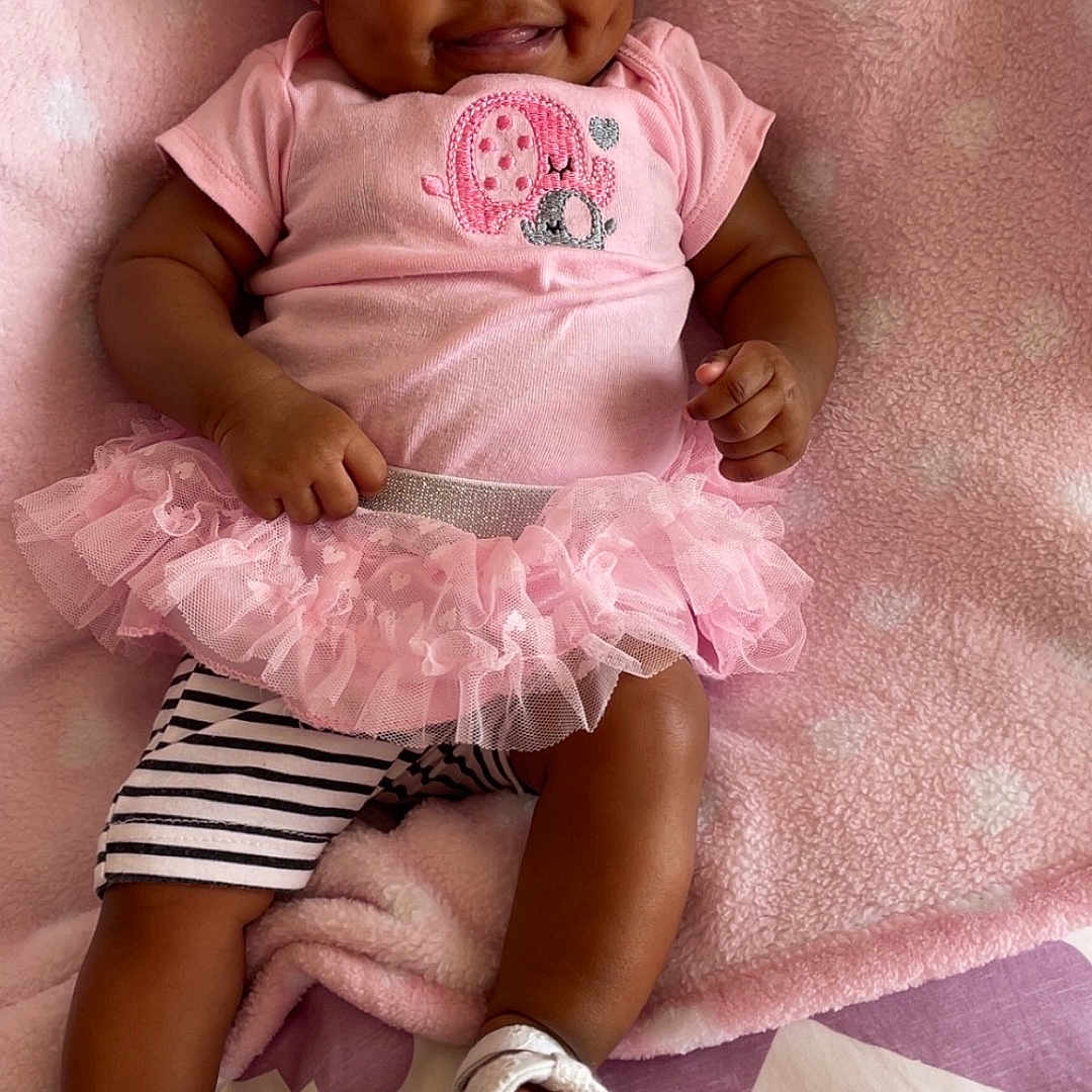Saeyora is registered to the contest to win money with this photo: baby, blanket, child, clothing, cute, dimples, fashion, footwear, happy, headband, indoors, infant, lying_down, person, pink, portrait, smiling, soft_texture, striped_shorts, tutu