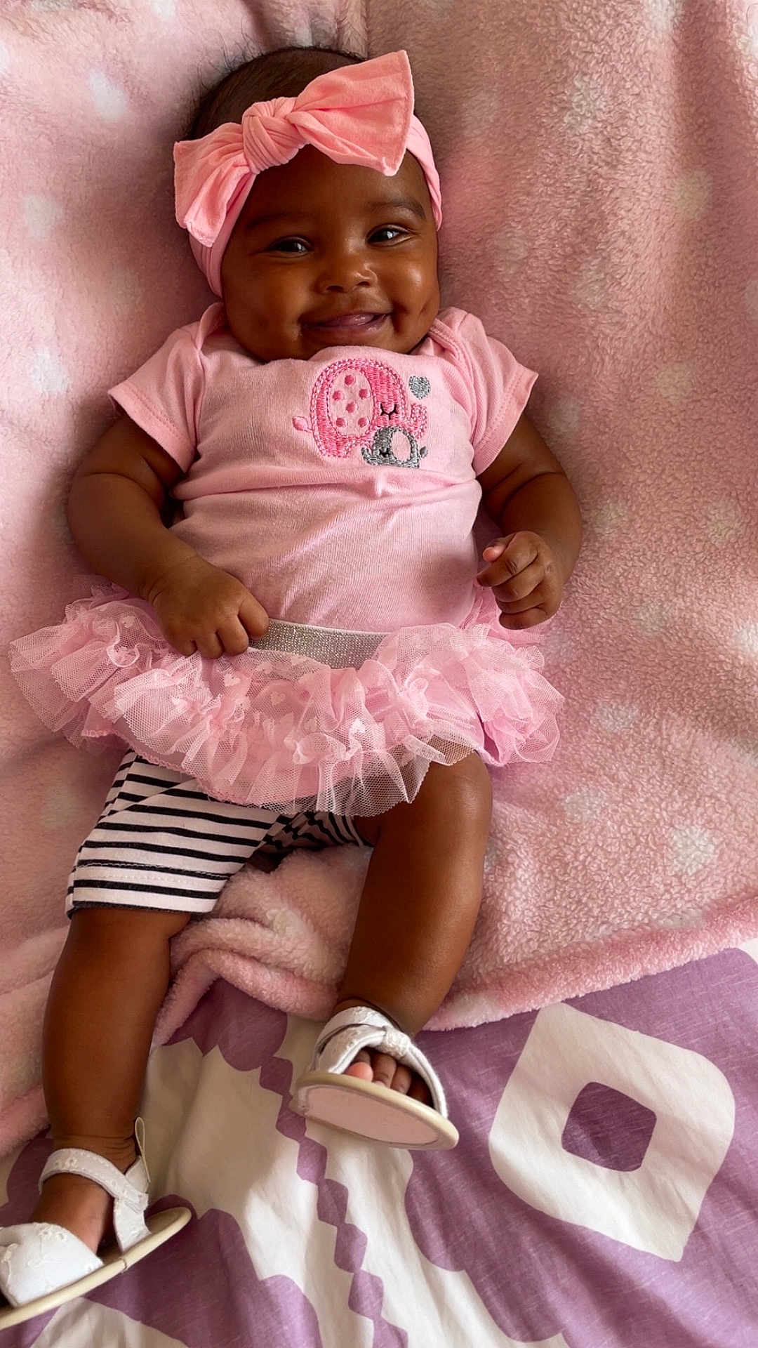 Saeyora is registered to the contest to win money with this photo: baby, smiling, pink, headband, tutu, blanket, cute, infant, dimples, clothing, footwear, striped_shorts, happy, lying_down, soft_texture, indoors, child, person, portrait, fashion
