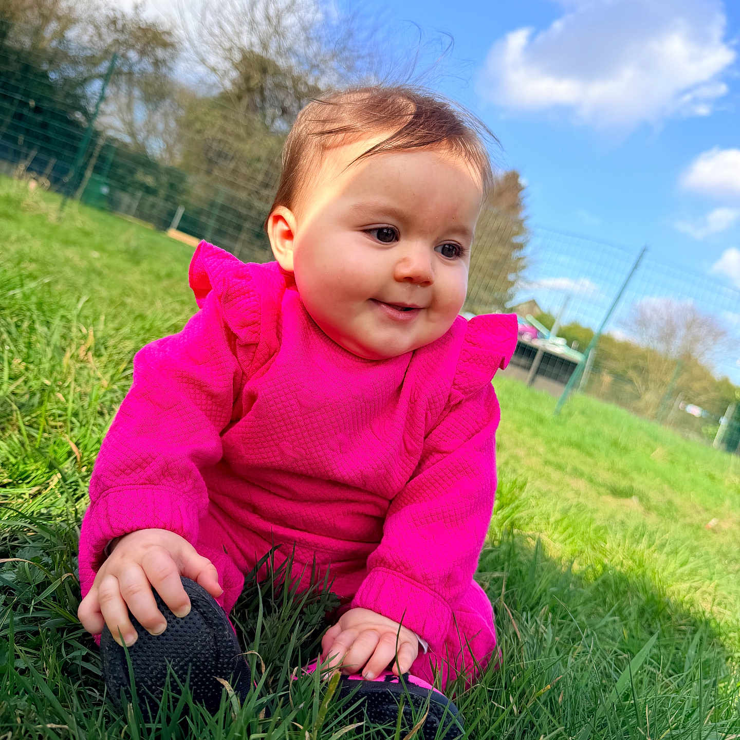 Atena a rejoint le concours — aidez-le/la à gagner de superbes lots ! baby, chubby_cheeks, clouds, cute, daylight, face, fence, grass, greenery, hand, infant, outdoors, park, pink_clothing, playful, portrait, shoe, sitting, sky, smile
