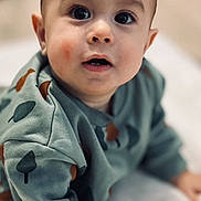 Kassim a rejoint le concours — aidez-le/la à gagner de superbes lots ! baby, child, infant, crawling, sweater, green_clothing, patterned_clothing, hand, face, wide_eyes, blanket, soft_texture, indoors, curious_expression, close_up, portrait, cute, young_child, head, skin