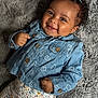 baby, smiling, denim_jacket, floral_pattern, pants, blanket, curly_hair, cute, happy, portrait, infant, clothing, child, face, hands, button, texture, cozy, lying_down, soft