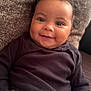 Myla is registered to the contest to win money with this photo: baby, smiling, curly_hair, face, child, infant, clothing, long_sleeve, couch, cushion, happy, portrait, person, skin, young_child, indoors, cute, relaxed, seated, toddler