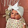 newborn, baby, infant, wrapped, blanket, floral_pattern, headwrap, bow, crocheted_toy, teddy_bear, pink_background, knitted, cozy, cute, portrait, hand, nail_polish, face, eyes, indoors