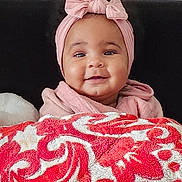 Janah a rejoint le concours — aidez-le/la à gagner de superbes lots ! baby, infant, smile, headband, pink_clothing, blanket, red_pattern, white_pattern, cozy, portrait, child, cute, happy, indoor, warm, soft_texture, face, person, young_child, headwear