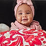 baby, infant, smile, headband, pink_clothing, blanket, red_pattern, white_pattern, cozy, portrait, child, cute, happy, indoor, warm, soft_texture, face, person, young_child, headwear