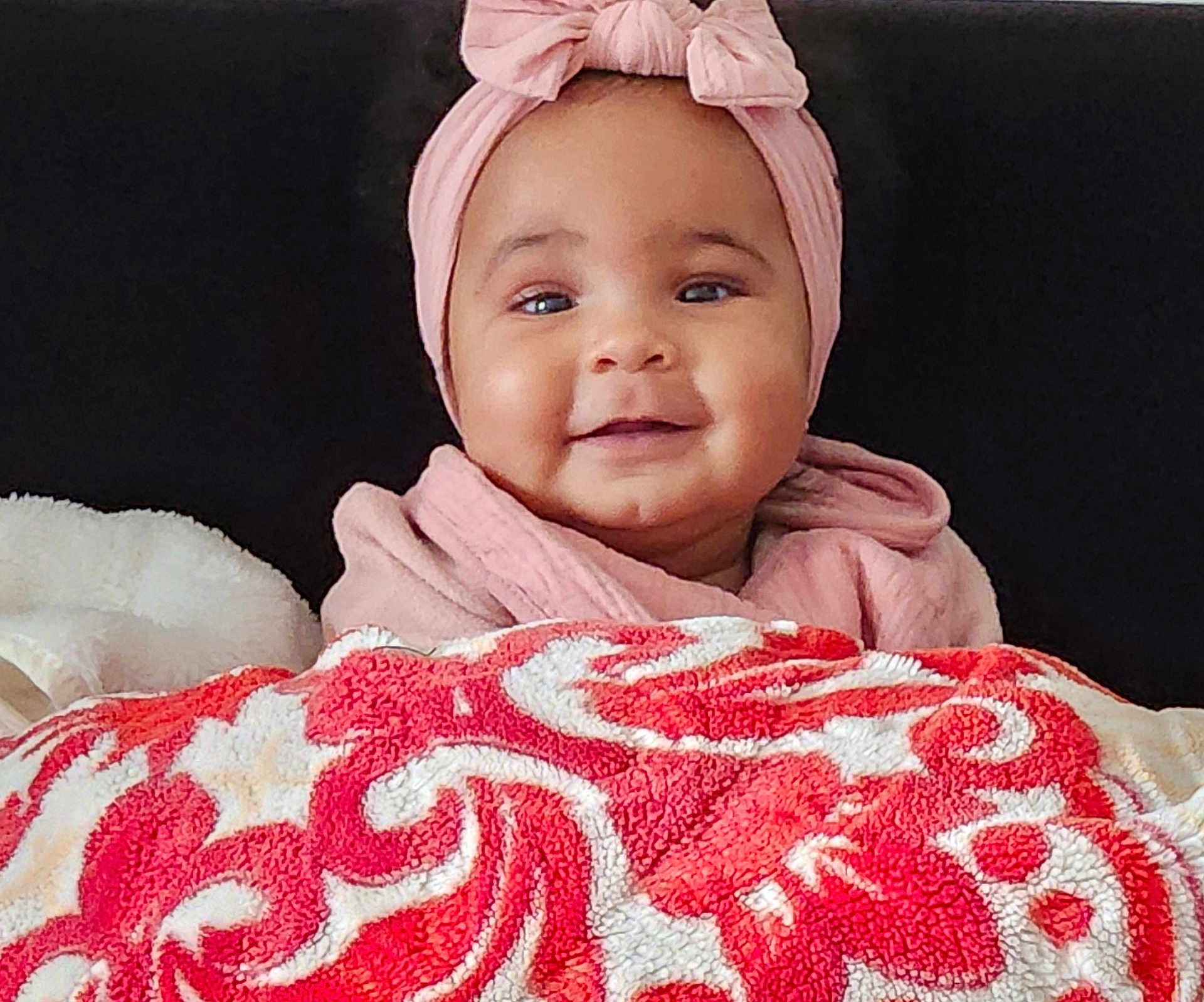 Janah a rejoint le concours — aidez-le/la à gagner de superbes lots ! baby, infant, smile, headband, pink_clothing, blanket, red_pattern, white_pattern, cozy, portrait, child, cute, happy, indoor, warm, soft_texture, face, person, young_child, headwear