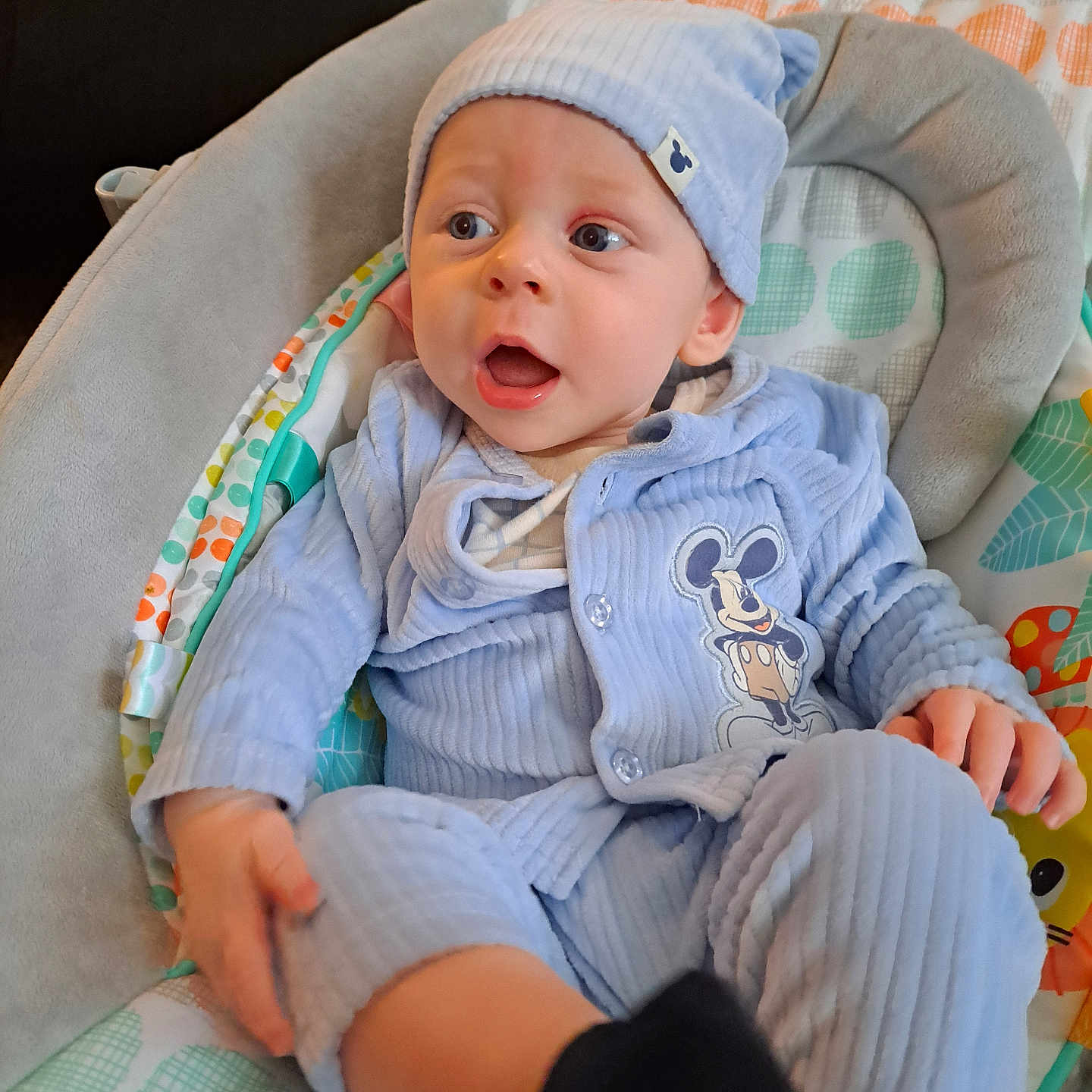River joined the competition — help win amazing prizes! baby, child, infant, portrait, blue_hat, blue_clothing, mickey_mouse, cushioned_seat, baby_chair, sitting, wide_eyed, open_mouth, indoors, colorful, blanket, patterned_fabric, hands, legs, cozy, happy