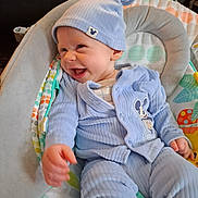 River is registered to the contest to win money with this photo: baby, infant, child, smiling, happy, portrait, blue_hat, blue_clothing, onesie, baby_bouncer, cushion, seated, indoors, home, colorful, patterned, mickey_mouse, close_up, joyful, photography