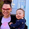 Bear is registered to the contest to win money with this photo: baby, child, adult, woman, portrait, smiling, happy, glasses, blue_door, brick_wall, front_porch, outdoor, family, holding, infant, clothing, navy_outfit, pink_shirt, seated, home