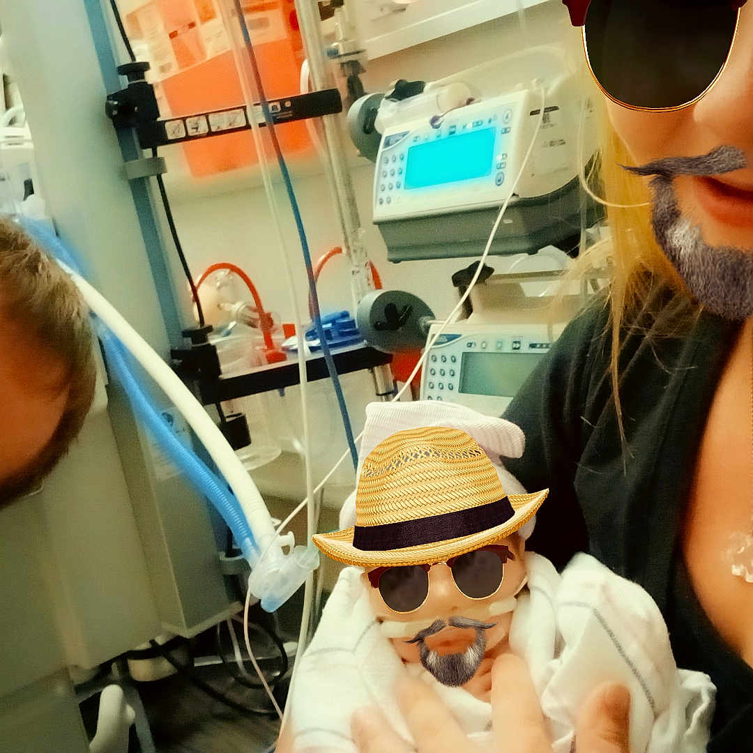 Delilah Rose Lynn is registered to the contest to win money with this photo: adult, baby, beard_filter, blanket, family, hat_filter, holding, hospital, man, medical_equipment, monitors, newborn, nicu, portrait, selfie, smile, sunglasses_filter, swaddle, tubing, woman