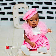 Nora joined the competition — help win amazing prizes! baby, toddler, child, pink_dress, beret, cushion, floor, tile_floor, indoor, portrait, black_and_white_background, letter_e, fashion, cute, sitting, person, clothing, footwear, studio_photography, expression