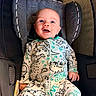 baby, child, infant, smiling, happy, blue_eyes, portrait, car_seat, buckled, seated, indoor, close_up, dinosaur, printed_clothing, onesie, automobile, travel, face, head, photography