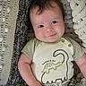 baby, smile, infant, face, clothing, dinosaur, striped_pants, blanket, texture, cute, child, portrait, happy, young, person, indoors, soft, cozy, button, casual