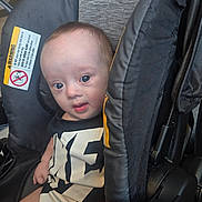 Roman is registered to the contest to win money with this photo: baby, baby_transport, black_clothing, child, close_up, clothing, eyes, face, indoors, infant, looking_at_camera, photograph, portrait, safety_label, seated, shirt, stroller, warning_sign, wide_eyed, yellow_accent