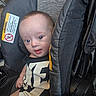 baby, baby_transport, black_clothing, child, close_up, clothing, eyes, face, indoors, infant, looking_at_camera, photograph, portrait, safety_label, seated, shirt, stroller, warning_sign, wide_eyed, yellow_accent