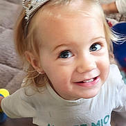 Love participe au concours pour gagner de l'argent avec cette photo : blonde_hair, blue_eyes, carpet, child, closeup, cute, earrings, face, happy, indoor, person, playful, portrait, smile, text_on_clothing, tiara, toddler, toy, white_shirt, young_child