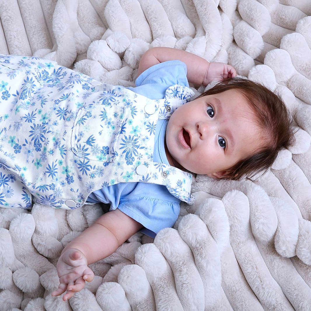 Deyna is registered to the contest to win money with this photo: baby, blanket, blue_clothing, child, curious_expression, cute, face, floral_pattern, hand, head, indoors, infant, lying_down, plush, portrait, skin, smiling, soft_texture, toddler, young