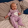 Hope is registered to the contest to win money with this photo: baby, infant, purple_onesie, cloud_design, bed, pillow, blanket, smiling, happy, infant_clothing, child, indoor, cute, person, sleepwear, soft_fabric, relaxing, lying_down, face, head
