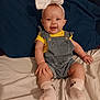 baby, child, smile, bow, headband, denim_overalls, yellow_shirt, socks, paws, bed, pillow, blue_pillow, happy, cute, infant, person, indoor, clothing, sitting, portrait