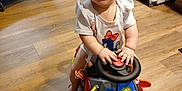 Hope joined the competition — help win amazing prizes! baby, child, toy_car, indoor, flooring, smiling, happy, steering_wheel, clothing, play, crawling, wooden_floor, pacifier, cabinet, water_bottles, refrigerator, playpen, colorful_toys, infant, cute