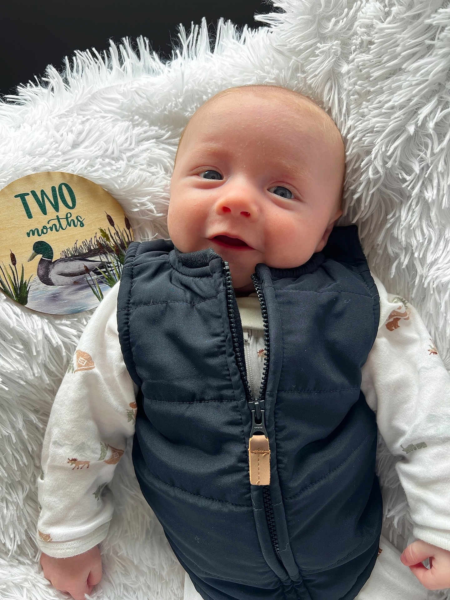 Luke joined the competition — help win amazing prizes! baby, infant, newborn, two_months, milestone, milestone_disc, smile, face, eyes, vest, zipper, onesie, blanket, faux_fur, hand, portrait, close_up, cozy, indoor, prop_sign