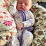 baby, sleeping, infant, onesie, floral_pattern, cushion, blanket, indoor, peaceful, soft_lighting, closeup, cute, child, person, relaxing, home, portrait, newborn, resting, cozy