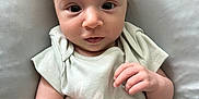 Elodie is registered to the contest to win money with this photo: baby, infant, face, hands, onesie, cushion, soft, curious, expression, skin, small_hands, lying_down, indoors, portrait, child, cute, wide_eyes, pale_clothing, human, newborn