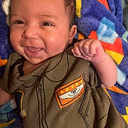 Kymani joined the competition — help win amazing prizes! baby, smiling, infant, clothing, blanket, fist, happy, face, person, cute, portrait, child, lying_down, colorful, soft, young, indoors, apparel, expression, infancy