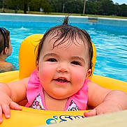 Kinsley joined the competition — help win amazing prizes! baby, child, pool, water, float, yellow, swimming, happy, smiling, wet_hair, outdoor, summer, fun, infant, pink_clothing, person, recreation, leisure, floating, background