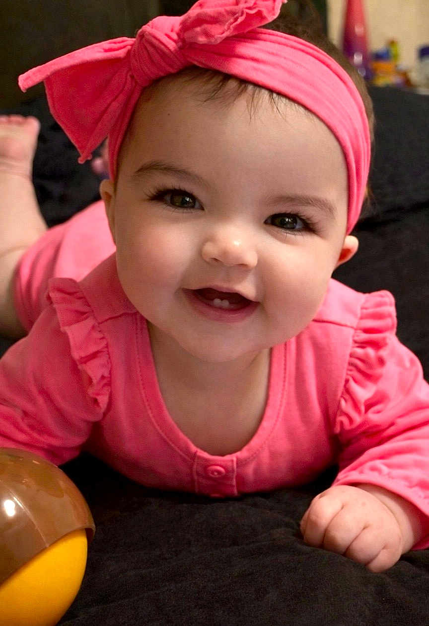 Kinsley is registered to the contest to win money with this photo: baby, infant, smiling, headband, bow, pink_outfit, rosy_cheeks, tooth, big_eyes, long_eyelashes, hand, toy, lying_down, portrait, close_up, indoor, blanket, happy, adorable, cute