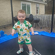 Landyn Scott is registered to the contest to win money with this photo: child, toddler, trampoline, dinosaur_pajamas, socks, standing, smiling, backyard, house, grill, fence, safety_net, grass, outdoor, portrait, red_hair, play, young_child, happy, clothing