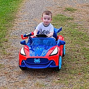 Landyn Scott is registered to the contest to win money with this photo: blue_car, casual_clothing, child, daylight, driving, fun, grass, gravel_path, lee_tshirt, nature, outdoor, person, playing, red_car, short_hair, smiling, toddler, toy_car, vehicle, young_child