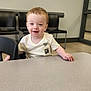 Landyn Scott joined the competition — help win amazing prizes! toddler, child, smiling, table, shirt, indoor, waiting_room, chairs, person, face, short_hair, light_skin, wood_floor, window, casual_clothing, expression, young_child, seated, hand, happy