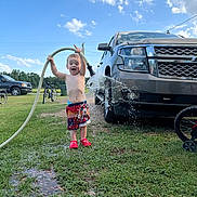 Landyn Scott joined the competition — help win amazing prizes! child, toddler, water_hose, water_splash, shorts, red_shoes, truck, grass, outdoor, daytime, sky, clouds, bicycle, joyful, playful, summer, greenery, vehicle, fun, nature