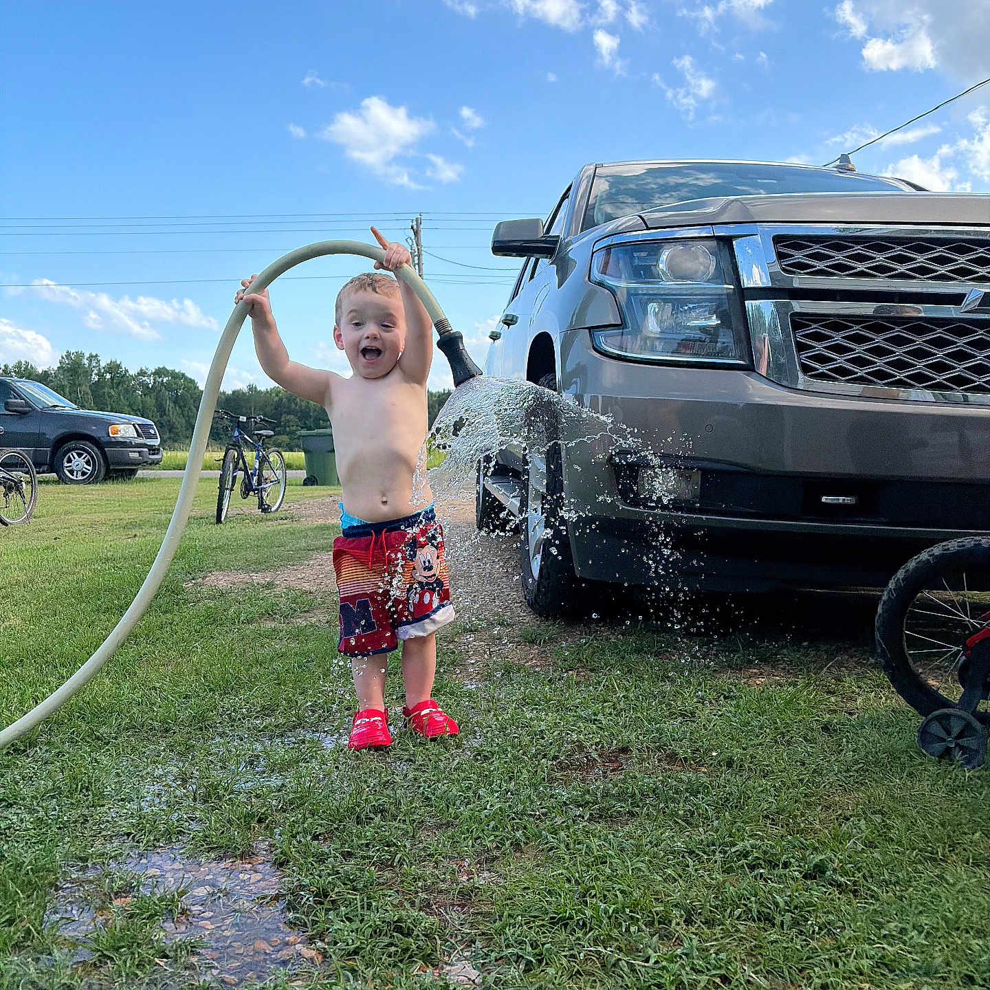 Landyn Scott joined the competition — help win amazing prizes! child, toddler, water_hose, water_splash, shorts, red_shoes, truck, grass, outdoor, daytime, sky, clouds, bicycle, joyful, playful, summer, greenery, vehicle, fun, nature