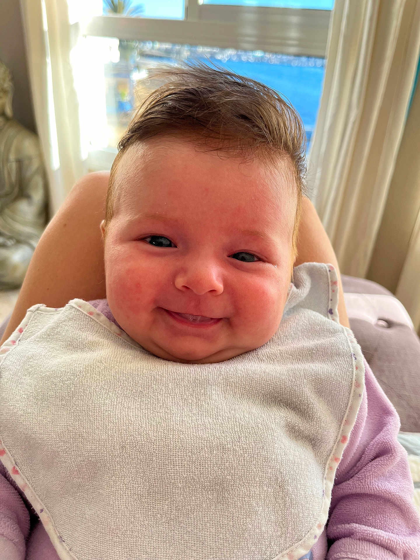 Alba participe au concours pour gagner de l'argent avec cette photo : baby, infant, smile, face, bib, clothing, purple_sleeves, cheeks, person, indoors, window, curtains, statue, buddha, light, skin, hair, closeup, happy, portrait