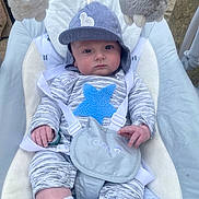 Rowan is registered to the contest to win money with this photo: baby, infant, child, pajamas, hat, blue_star, baby_seat, toy, plush_toy, gray_clothing, white_socks, face, person, indoor, cushion, straps, cute, small_hands, expression, seated