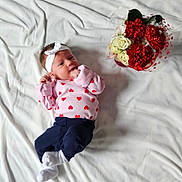 Alaina is registered to the contest to win money with this photo: adorable, baby, cozy, curious_look, cute, decorative_wrapping, flower_bouquet, headband, heart_pattern, indoor, infant, lying_down, navy_pants, pink_shirt, portrait, red_flowers, small_hands, soft_lighting, white_blanket, white_flowers