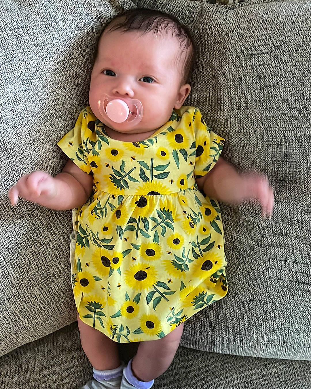 Lila is registered to the contest to win money with this photo: arm, baby, baby_toddler_clothing, cheek, day_dress, dress, face, finger, head, iris, neck, one_piece_garment, pattern, person, pink, product, skin, sleeve, standing, textile