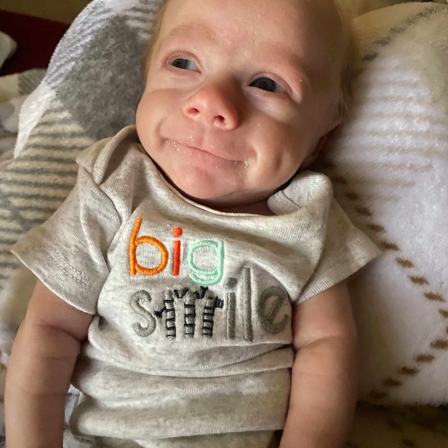 Mateo joined the competition — help win amazing prizes! baby, infant, smile, onesie, clothing, blanket, soft, cute, face, expression, cheek, arm, sitting, comfort, indoors, person, human, child, happy, young