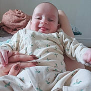 Alès Kylian participe au concours pour gagner de l'argent avec cette photo : baby, blanket, cactus_pattern, child, clothing, cozy, cute, fingers, hand, happy, holding_hand, indoor, infant, lying_down, onesie, person, portrait, skin, smile, tongue_out