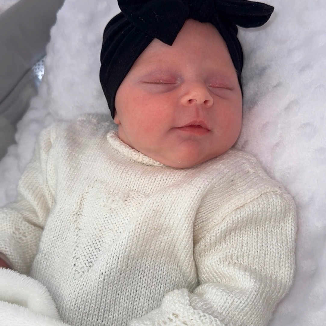 Hélyna participe au concours pour gagner de l'argent avec cette photo : baby, sleeping, infant, knit_sweater, black_bow, headband, blanket, bassinet, soft_texture, cozy, cute, child, indoors, peaceful, newborn, portrait, white, resting, comfort, warm