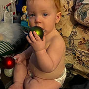 Ezra joined the competition — help win amazing prizes! baby, child, diaper, christmas_ornament, green_ball, red_ball, floor, indoor, curious, sitting, decor, holiday, toy, face, hand, feet, furniture, couch, plush, person