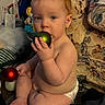 baby, child, diaper, christmas_ornament, green_ball, red_ball, floor, indoor, curious, sitting, decor, holiday, toy, face, hand, feet, furniture, couch, plush, person